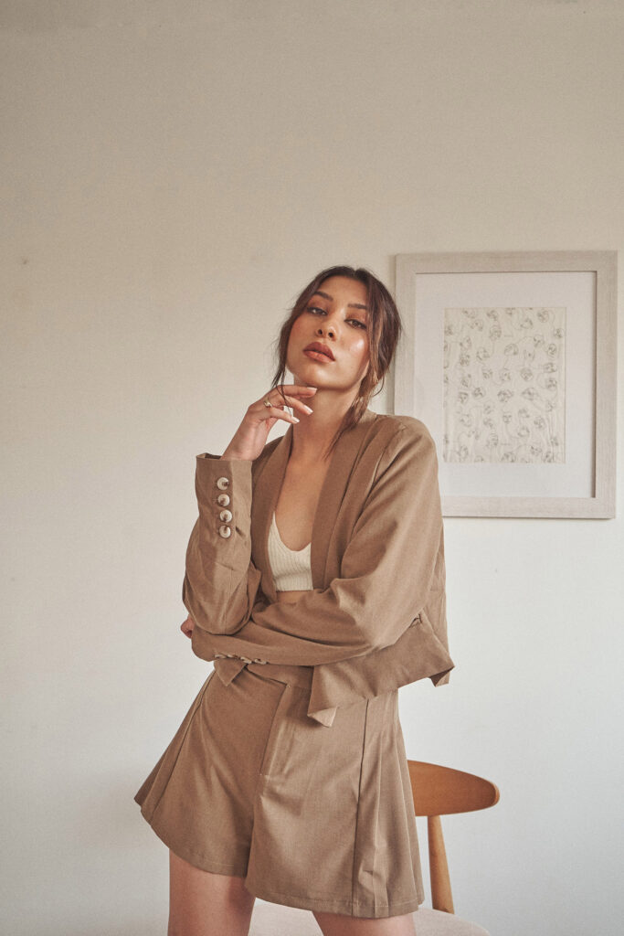 Nadya Inzunza is shown in a poised pose wearing a beige blazer and shorts with a framed artwork in the background.
